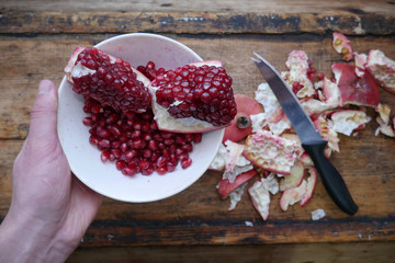 man holds a plate with sliced pomegranate and pomegranate fruits in a white plate, near the rind from pomegranate on a wooden dark background
