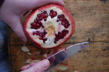 man cuts a ripe pomegranate with a knife on  wooden background