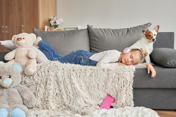 Girl and dog laying on couch in headphones, listening to music with her smarthphone. Little girl watching cartoons on her phone. Listening to an audiobook