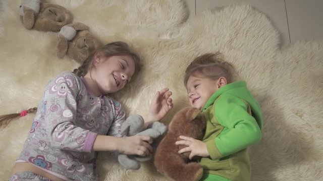 Siblings rolling on the fluffy carpet. Brother and sister have a fun. Happy kids weekend. Slow motion.