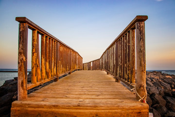 Obraz premium The wooden bridge overlooking the sea leads to an island at sunset.