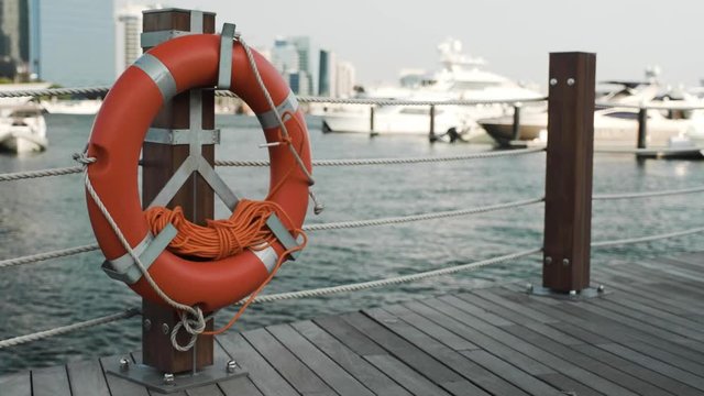 close view wooden pier with red safety buoy on post against large white luxury cruise yachts in Dubai sea bay
