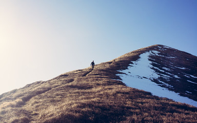 One Man hiker hiking alone climbing down a steep mountain path in winter. Taken from distance....