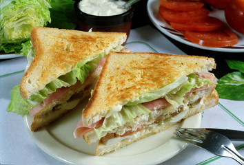 Plato con un sandwitch con pan de molde tostado, lechuga, tomate, jamón cocido y queso.