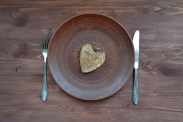 Flat view of wooden heart on plate. Romantic symbol. Dinner plate background. Valentine decoration.