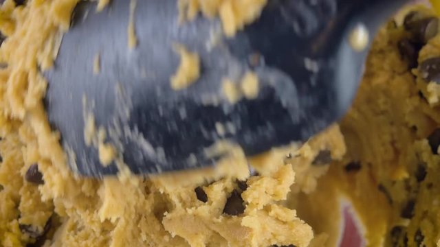 Macro shot of mixing raw chocolate chip cookie dough in 4k. A black, silicone spatula stirs incorporates bittersweet chocolate morsels. Extreme closeup for step by step recipes and homestyle baking.