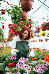 Redhead young woman working in greenhouse and enjoying in beautiful flowers. Female worker working at garden center.