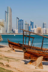 View of the skyline of Abu Dhabi from the Marina Breakwater beach with wooden boats, United Arab Emirates
