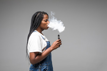 Portrait of guy holding vape device and exhaling cloud of smoke isolated on blue background.