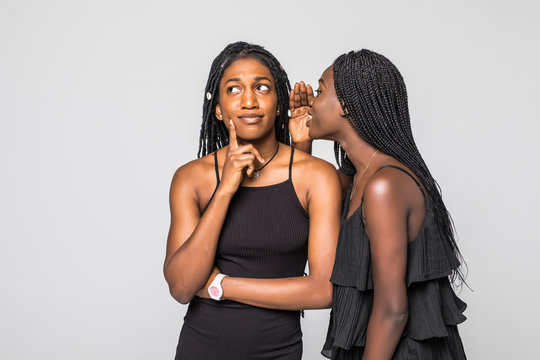Portrait of two happy young african women sharing secrets isolated on gray background
