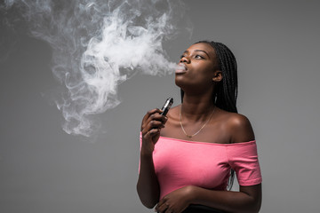 Young beauty african woman smoke vape, e-cigarette, isolated on gray background