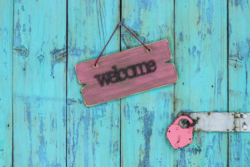 Wood welcome sign hanging on rustic teal blue wooden door with padlock