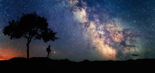 Photo sur Plexiglas Blue nuit Femme sous arbre regardant les étoiles et la Voie Lactée. Paysage de paysage avec ciel étoilé de nuit et silhouette de femme debout. Voie lactée avec voyageur. Univers.