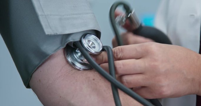 Extreme close up on hands of doctor using blood pressure cuff on patient