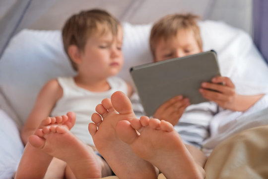 Two boys holding smartphone, tablet sitting on chair, focus on childrens feet.