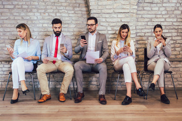 Business people waiting for job interview. They use their phones while waiting