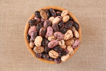 Raw purple, pink, beige with brown speckled kidney beans in wooden bowl at raw linen cloth. Closeup