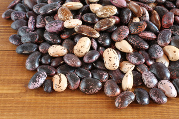 Raw purple, pink, beige with brown speckled kidney beans on brown wooden table. Closeup