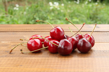 Ripe dark red cherries on a brown wooden table against green grass background