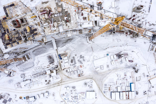 construction area in winter, aerial top view. tower cranes and equipment building new apartments in snow