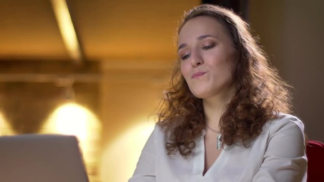 Close-up portrait of young curly-haired woman reclines on chair with satisfaction in office.