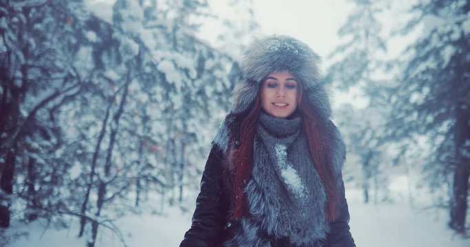 Beautiful and happy woman walks in the winter forest. There is snow in the trees. Girl is wearing a winter hat, jacket and mittens.