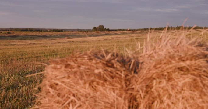 a haystack on a field, in the background an old tractor drives away