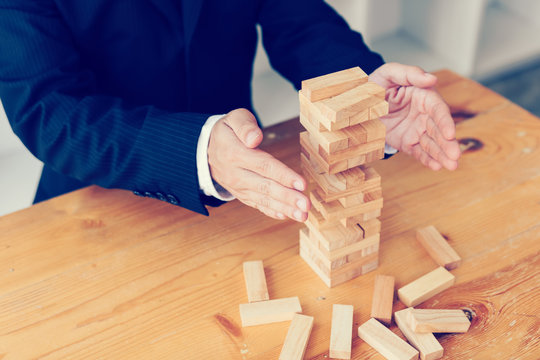 Hands of businessman protect block wooden on table with risk concept.