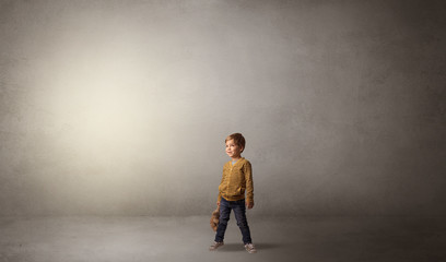 Obraz premium Little waggish kid staying alone in a big empty room with his plush 