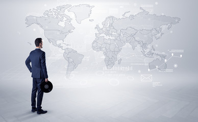 Businessman standing with his back and looking at a worldwide map with objects in his hand
