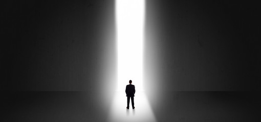 Businessman standing and seeing the light at the end of a big wall
