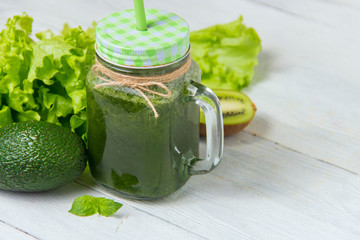 Healthy green smoothie with ingredients on white wooden background