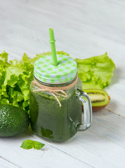Healthy green smoothie with ingredients on white wooden background