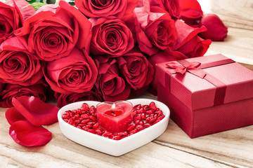 Obraz na płótnie Canvas Festive background to the Valentine's day. A bouquet of red roses, a gift box, a heart-shaped plate and a heart-shaped candle. On a wooden background.