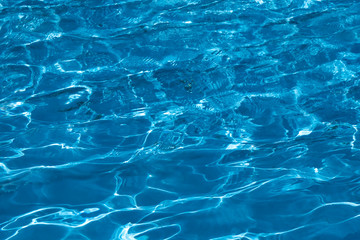 Fototapeta na wymiar Blue and bright ripple water surface in swimming pool with sun reflection.