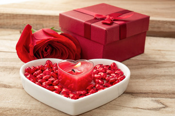 Festive background to the Valentine's day. Flower rose, gift box, a heart-shaped plate and a heart shaped candle. On a wooden background.