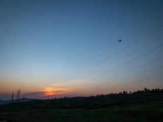 Field after sunset with power lines with flying aircraft