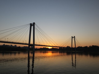 Fototapeta na wymiar Suspension bridge over the river, illuminated by the setting sun in Krasnoyarsk city