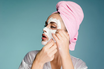 beautiful young girl with a pink towel on her head removes a white nourishing mask from her face