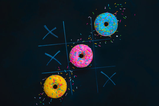 Glazed donuts tic-tac-toe game. Chalk drawing on a dark background with copy space. Creative food flat lay.
