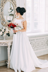 Fototapeta na wymiar Bride in a bright Studio with a bouquet. Wedding dress and mirror.