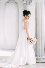 Fototapeta premium Beautiful girl in a wedding dress with a bouquet. Bride in a bright Sunny Studio.