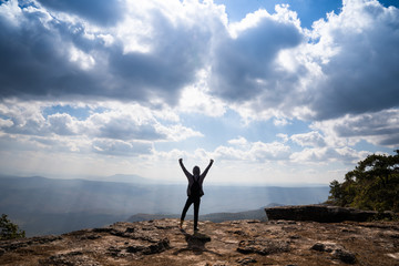 A person hands up standing on rocky mountain looking out at scenic natural view and beautiful blue sky