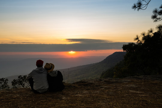 Image of sunrise or sunset on orange and yellow horizon with a silhouette of a couple in natural surrounding