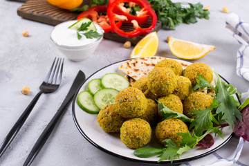 Homemade spicy chickpea falafel garnished with fresh vegetable and yogurt on a plate over light concrete background. Israeli cuisine concept