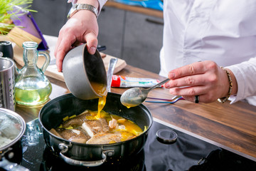 Chef adds sauce to the pan with halibut. Master class in the kitchen. The process of cooking. Step by step. Tutorial. Close-up