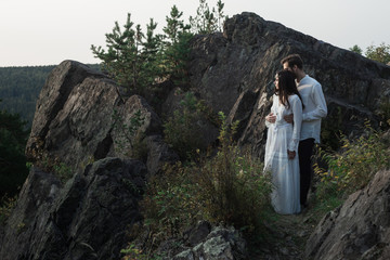 Beautiful couple in love walks in the mountains, against the backdrop of rocks, in the rays of the setting sun. man and woman love each other, they are gentle and happy, a love story and a wedding day