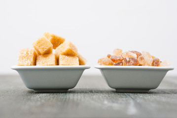 brown cubes and rock sugar on white square dishes, dark wood table