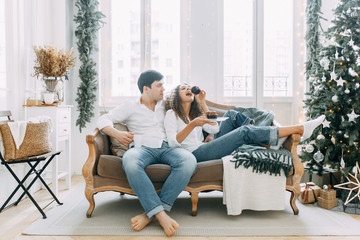Obraz premium A young couple lying on the couch in an embrace. Photo shoot in a bright interior Studio for the New year.