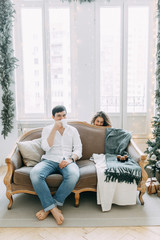 Obraz premium A young couple lying on the couch in an embrace. Photo shoot in a bright interior Studio for the New year.